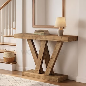 May include: A wooden console table with a natural finish. The table has a rectangular top supported by a V-shaped base. A small lamp and books are on the table. A mirror hangs on the wall behind the table. The table is approximately 150 cm long.