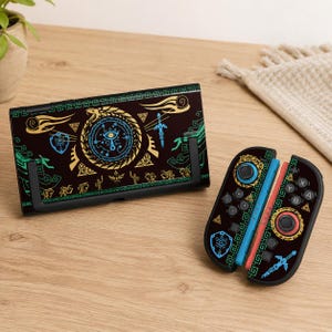 May include: A black Nintendo Switch dock and Joy-Cons featuring a gold, teal, and blue design. The design includes a central emblem, swords, and other decorative elements. The Joy-Cons are red and blue.