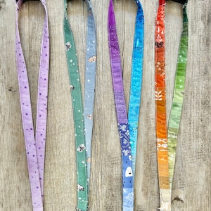 May include: A collection of five fabric lanyards with various patterns. The lanyards feature a black plastic clasp and a silver metal swivel hook. Patterns include stars, clouds, insects, a lighthouse, and a gradient of colors.