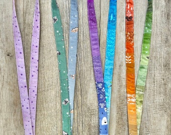 May include: A collection of five fabric lanyards with various patterns. The lanyards feature a black plastic clasp and a silver metal swivel hook. Patterns include stars, clouds, insects, a lighthouse, and a gradient of colors.