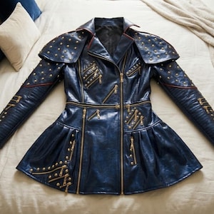 May include: A dark blue leather jacket with gold-colored zippers and stud accents. The jacket features a fitted waist, flared skirt, and shoulder pads. The sleeves are long and detailed with additional studs and zippers. The jacket is laid flat on a bed.