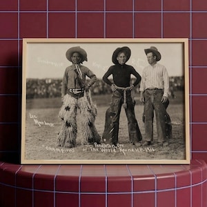 Puede incluir: Una fotografía en blanco y negro en un marco de madera clara que muestra a tres personas con atuendo de vaquero de pie en un campo. El texto en la imagen dice Lee Moorhouse, Champions of the World, Pendleton, Ore, 1916, y otros nombres.