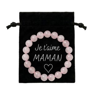Peut inclure: Un sac en velours noir avec un bracelet de perles en quartz rose. Le sac porte l'inscription "Je t'aime MAMAN" en écriture blanche, ainsi qu'un symbole de cœur. Le bracelet est composé de perles roses claires et rondes.