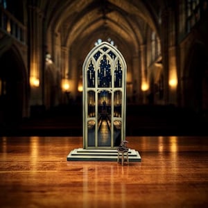 Puede incluir: Una ventana arqueada en miniatura detallada, que representa una escena interior, colocada sobre una base rectangular. El marco de la ventana es de color claro, con un diseño de cielo nocturno azul oscuro. Un pequeño sombrero marrón está sobre un pequeño taburete.