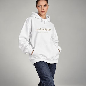 May include: A white hooded sweatshirt with long sleeves, a front kangaroo pocket, and a drawstring hood. The chest features the word PHASER printed in a stylised gold font, accompanied by smaller text and graphic symbols underneath the main logo.