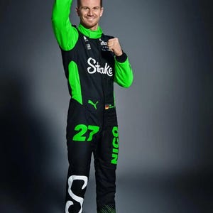 Puede incluir: Un traje de carreras negro y verde neón con el texto Stake, el número 27 y el nombre Nico. El traje incluye un logotipo de Puma, un pequeño emblema de la bandera alemana y zapatillas deportivas a juego en verde neón y negro con cordones.