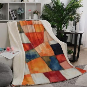 Può includere: Una coperta in peluche con un design patchwork di quadrati in stile acquerello nei toni dell'arancione, rosso, blu e crema. La coperta presenta una spessa fodera in pile sherpa bianco testurizzato visibile lungo i bordi e la superficie.