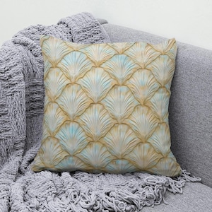 May include: A square throw cushion featuring a repeating pattern of fan-shaped, shell-like motifs in shades of soft gold, beige, and pale blue. The design creates a textured, layered appearance across the entire surface of the fabric cushion.