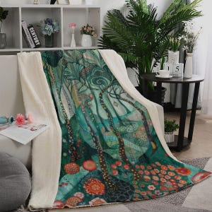 May include: A plush throw blanket featuring a vibrant forest illustration with tall, patterned trees in shades of teal and green, accented by orange and red circular floral motifs, finished with a thick, cream-coloured sherpa fleece lining.