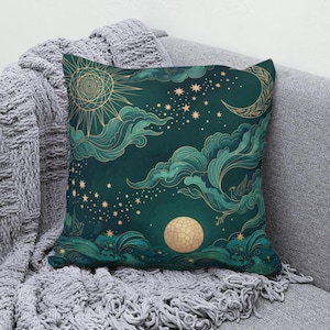 May include: A square throw pillow featuring a dark teal background with a celestial design. The print includes a golden sun, a crescent moon, a full moon, and numerous stars scattered among swirling teal clouds and stylized bird silhouettes.