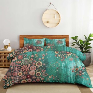 Könnte beinhalten: Ein Bettwäscheset mit einem blaugrünen Hintergrund und einem Muster aus rosa und orangefarbenen kreisförmigen Motiven sowie stilisierten Blumen. Das Design umfasst einen Bettbezug und zwei passende Kissenbezüge mit aquarellartiger Textur.