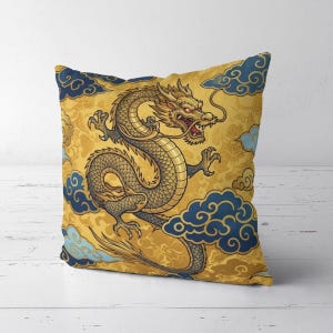 Könnte beinhalten: Ein quadratisches Dekokissen mit einer Illustration eines goldenen Drachen mit scharfen Krallen und einem langen Schwanz. Der Drache ist von dunkelblauen und hellblauen stilisierten Wolken vor einem gelben Hintergrund mit floralem Muster umgeben.