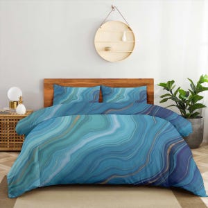May include: A bedding set featuring a duvet cover and two matching pillowcases with a blue and teal agate-inspired pattern. The design displays fluid, wavy lines in shades of light blue, deep navy, and turquoise, accented by thin gold veins.