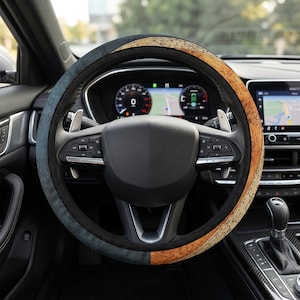 Puede incluir: Una funda para volante con un diseño dividido que presenta una sección texturizada de color azul oscuro a la izquierda y una sección con patrón de veta de madera de color marrón claro a la derecha, instalada sobre un volante negro.