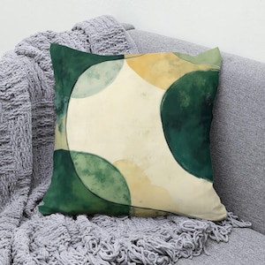 May include: A square throw pillow featuring an abstract watercolor design with large, overlapping circular shapes in shades of deep forest green, muted sage, and soft cream, accented by warm golden yellow patches across the surface.