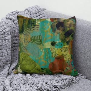 May include: A square throw pillow featuring an abstract collage design with layered shapes in shades of teal, olive green, mustard yellow, and burnt orange. The surface includes graphic patterns of concentric circles and dots over textured areas.