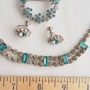 May include: A vintage jewelry set with a necklace, earrings, and a brooch. The set features clear and light blue rhinestones in a silver tone metal.