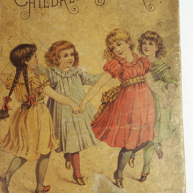 May include: Four young girls in dresses are holding hands and dancing in a circle. The girls are wearing yellow, blue, red, and green dresses. The background is a light brown color.