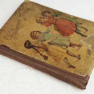 May include: A vintage book titled "Children's Hour" with a brown cover and illustrations of three girls in dresses playing. The book has a worn and aged appearance.