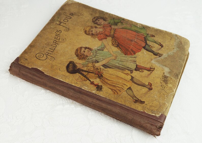 May include: A vintage book titled "Children's Hour" with a brown cover and illustrations of three girls in dresses playing. The book has a worn and aged appearance.