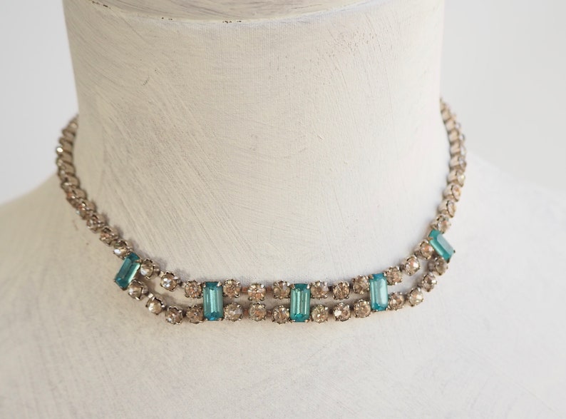 May include: A silver choker necklace with a double row of clear rhinestones and a row of rectangular turquoise blue stones.