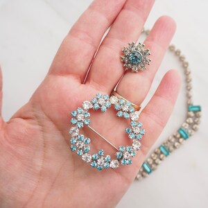 May include: A set of three vintage brooches featuring a circular design with blue and clear rhinestones. The brooches are made of silver tone metal and have a delicate, feminine style.