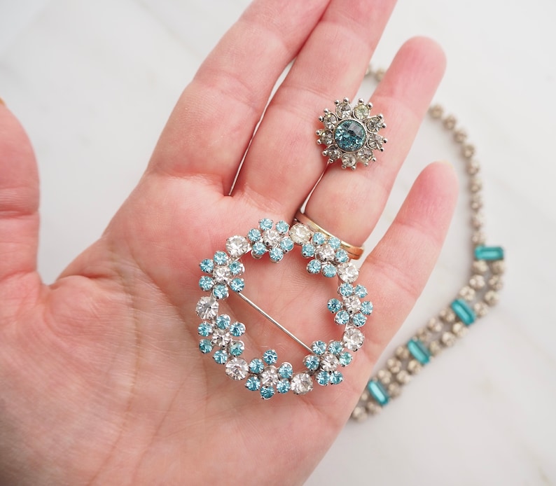 May include: A set of three vintage brooches featuring a circular design with blue and clear rhinestones. The brooches are made of silver tone metal and have a delicate, feminine style.