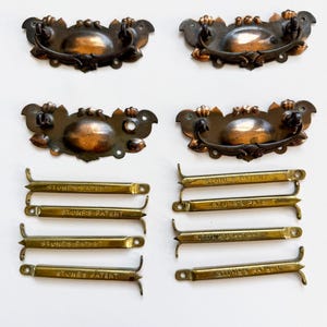 May include: Set of antique bronze drawer pulls and matching hardware. The pulls have a decorative floral design and are paired with brass-toned metal brackets. The text "STONE'S PATENT" is visible on the brackets.