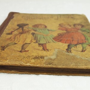 May include: A vintage children's book with a brown cover and a faded illustration of three girls in dresses dancing. The title of the book is "Children's Hours".