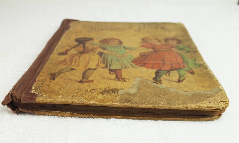 May include: A vintage children's book with a brown cover and a faded illustration of three girls in dresses dancing. The title of the book is "Children's Hours".
