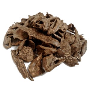 Puede incluir: Un montón de virutas de madera de oud marrón, con formas y texturas variadas, sobre un fondo blanco. Las piezas de madera tienen un aspecto natural y envejecido. La imagen incluye el texto "SABILY COLLECTION".