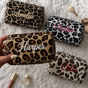 May include: Four rectangular corduroy cosmetic bags featuring leopard print patterns in various colorways. Each bag is embroidered with a name in cursive script: Amelia, Sophia, Harper, and Chloe. The bags are arranged on a textured white surface.