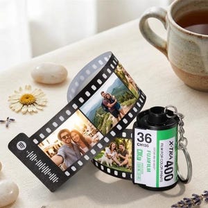 May include: A personalized photo film strip with attached film canister keychain. The black film strip displays multiple photos and a Spotify code. The film canister is black with a green label that reads "X-TRA 400" and "FUJIFILM".