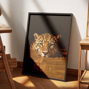 May include: A rectangular framed wall art print featuring a detailed illustration of a leopard with golden fur and black spots partially submerged in dark water. The leopard is looking forward with a calm expression, and the artwork is encased in a thin black frame.