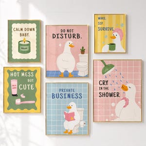 May include: A set of six framed art prints with whimsical illustrations. The prints feature a white duck in various bathroom-related scenarios, with text like "Calm Down Baby" and "Do Not Disturb." The color palette includes green, pink, and blue.