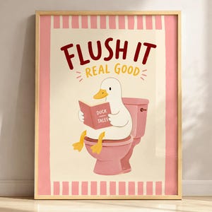Può includere: Una stampa artistica incorniciata raffigurante un'anatra bianca seduta su un water rosa che legge un libro intitolato Duck Tales. Il testo FLUSH IT REAL GOOD è stampato in rosso scuro e giallo sopra l'anatra. Il bordo ha strisce verticali rosa e bianche.