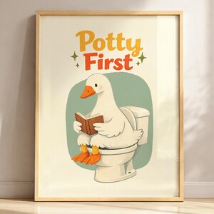 May include: A framed wall art print featuring a white goose with orange feet and beak sitting on a white toilet while reading a brown book. The text Potty First is printed in yellow and orange above the goose, accented by four small green stars.