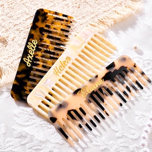 May include: Three rectangular hair combs with wide teeth. One comb is dark brown tortoise shell with the name Axelle in gold. The second is a cream-colored marbled comb with the name Helen in gold. The third is a light tortoise shell comb with the name Elaine in gold.