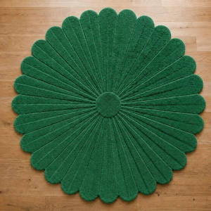 Puede incluir: Una alfombra circular de color verde intenso s&oacute;lido, con una superficie texturizada que presenta un patr&oacute;n radial de segmentos alargados en forma de p&eacute;talos que se extienden desde un n&uacute;cleo central circular, creando una silueta de flor.