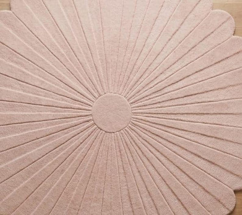 A close-up view shows the center and textured petal details of a pale pink scalloped flower rug.