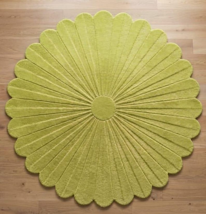 Puede incluir: Una alfombra circular de color verde lima vibrante, con una superficie texturizada y un patr&oacute;n radial de segmentos alargados en forma de p&eacute;talos que se extienden desde un centro circular s&oacute;lido, creando una silueta en forma de flor.