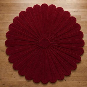 Puede incluir: Una alfombra circular de color rojo intenso con forma de flor, compuesta por numerosos p&eacute;talos redondeados que irradian desde un disco central s&oacute;lido. La alfombra presenta una superficie texturizada y est&aacute; extendida en plano.