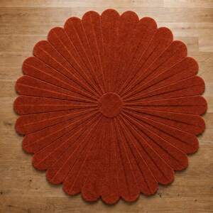 Puede incluir: Una alfombra circular de color naranja quemado intenso, que presenta un n&uacute;cleo central redondo con numerosos segmentos radiantes en forma de p&eacute;talos que se extienden hacia afuera para crear una silueta floral con una superficie texturizada.