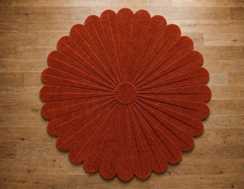 Puede incluir: Una alfombra circular de color naranja quemado intenso, que presenta un n&uacute;cleo central redondo con numerosos segmentos radiantes en forma de p&eacute;talos que se extienden hacia afuera para crear una silueta floral con una superficie texturizada.