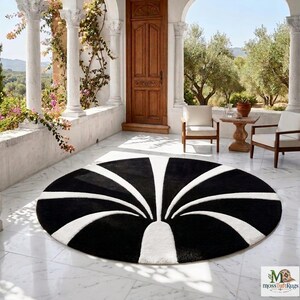 May include: A circular rug featuring a high-contrast black and white pattern with radiating curved lines that originate from a central base, creating a stylized fan or fountain design on a smooth, light-colored marble floor surface.
