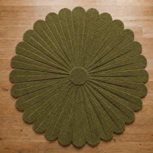 Puede incluir: Una alfombra circular de color verde oliva con una superficie texturizada y copetuda, que presenta un patr&oacute;n radial de segmentos alargados en forma de p&eacute;talos que se extienden desde un centro redondo y s&oacute;lido, formando una flor.