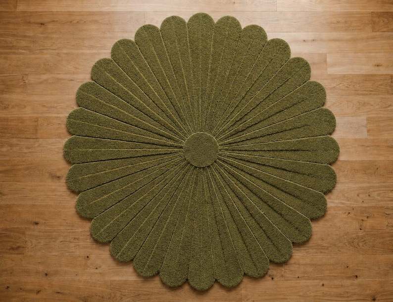 Puede incluir: Una alfombra circular de color verde oliva con una superficie texturizada y copetuda, que presenta un patr&oacute;n radial de segmentos alargados en forma de p&eacute;talos que se extienden desde un centro redondo y s&oacute;lido, formando una flor.