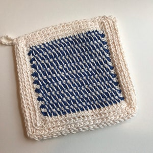 Puede incluir: Un posavasos de ganchillo blanco con un centro a cuadros azul y blanco. El posavasos tiene un lazo para colgar.