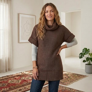 Puede incluir: Una túnica de punto marrón oscuro con cuello tipo chimenea, mangas cortas con puños doblados y un dobladillo acanalado. La prenda se lleva sobre una camiseta gris claro de manga larga y se combina con pantalones vaqueros azules.