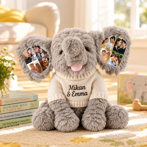 Könnte beinhalten: Ein graues Plüschelefant-Spielzeug, das einen cremefarbenen Strickpullover mit dem aufgedruckten Text Mikan & Emma trägt. Der Elefant hat große Ohren mit Fotocollagen von Paaren, einen weichen Rüssel und eine kleine rosa Zunge.
